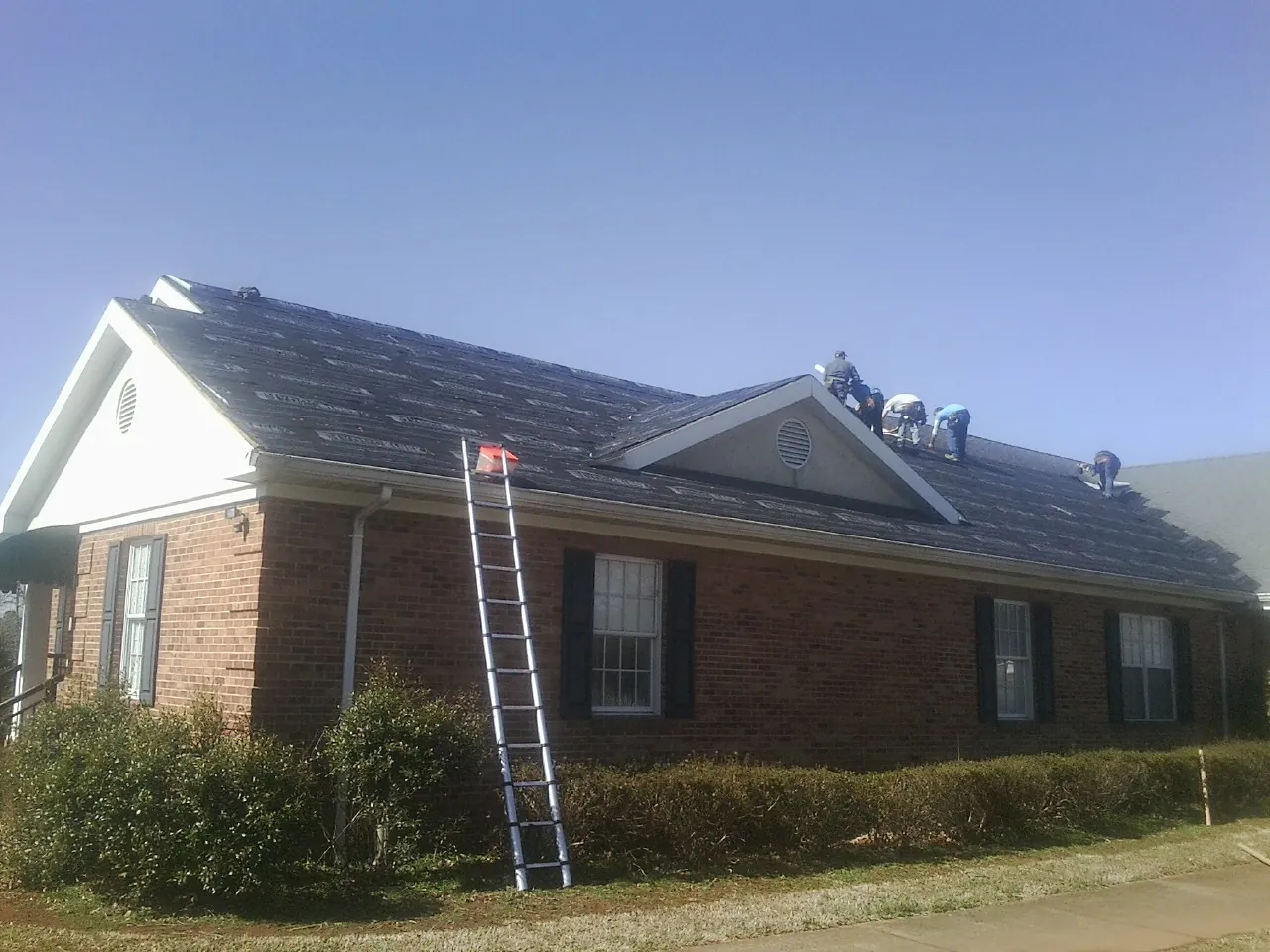Crew tearing shingles off a brick ranch roof with a ladder set — Metal Roof Repair work by our crew in Welcome