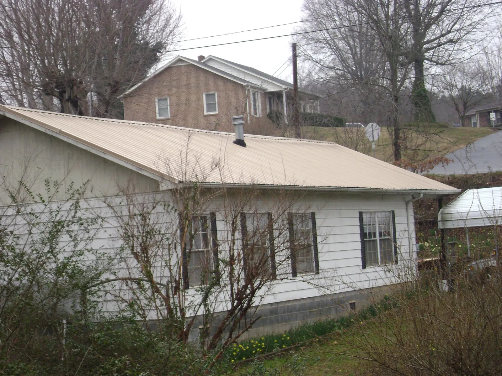 Tan metal roof on a white sided house set into a hillside — Commercial Roofing by Roofing Brothers in Welcome
