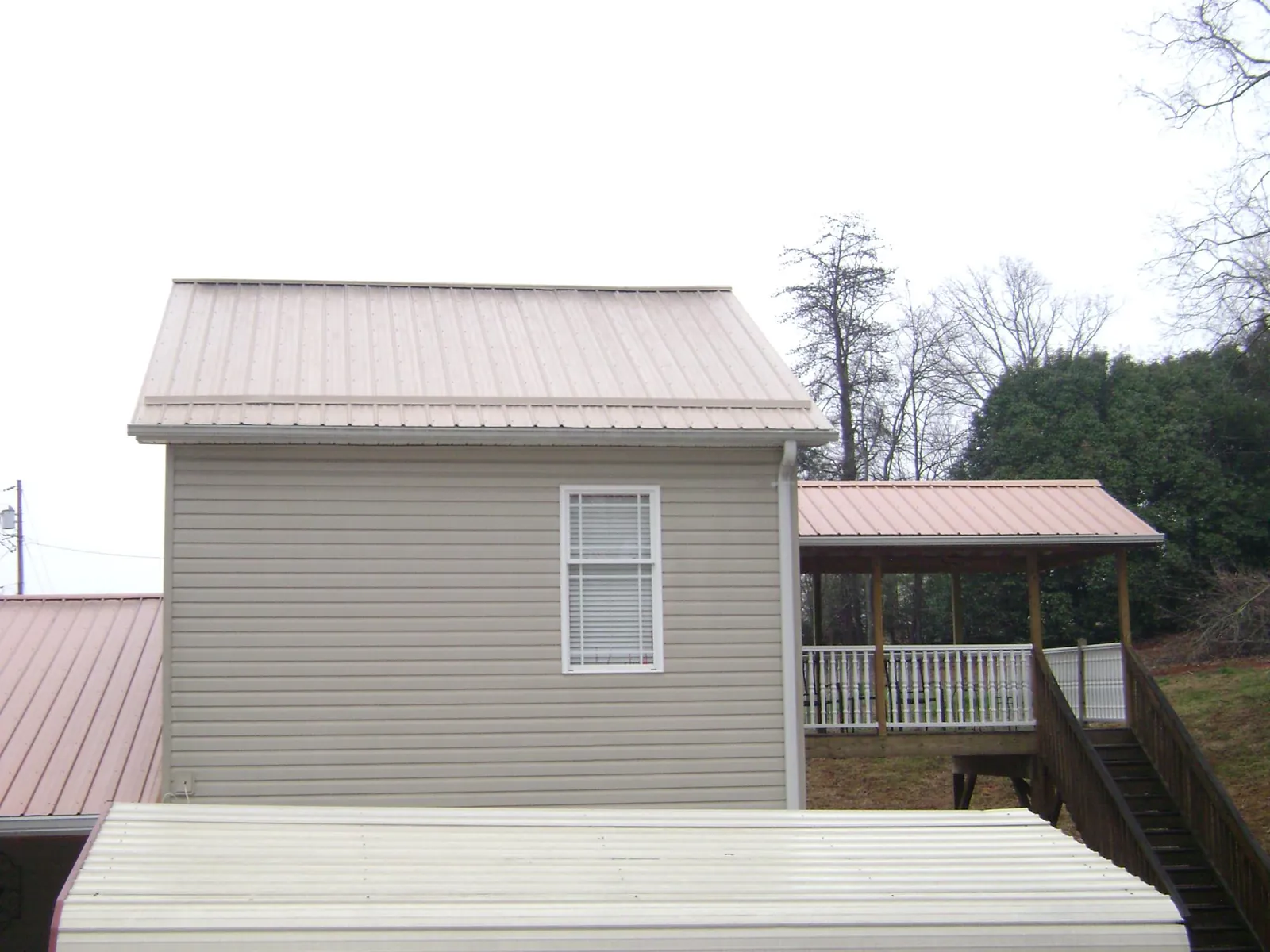 Tan metal roofs on a two story addition and attached porch, from a Roof Replacement job in Welcome